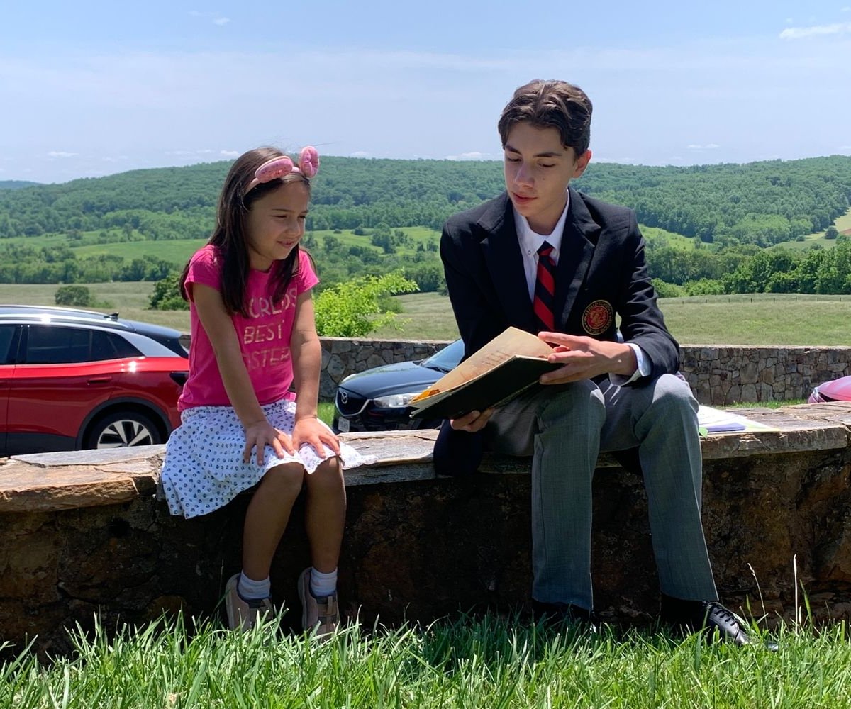 upper school student sitting outside reading to lower school student